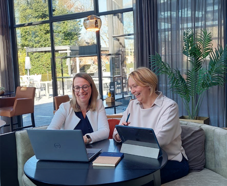 Zwei Frauen lächeln und schauen auf einen Laptop in einer Hotellobby.