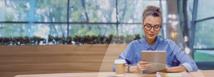 Avendra International-Mitarbeiterin, die an einem modernen, gut beleuchteten Tisch mit einer Kaffeetasse ein Tablet benutzt.