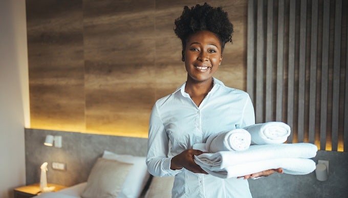 Hotelpersonal posiert mit einem Stapel weißer Handtücher in einem Hotelzimmer