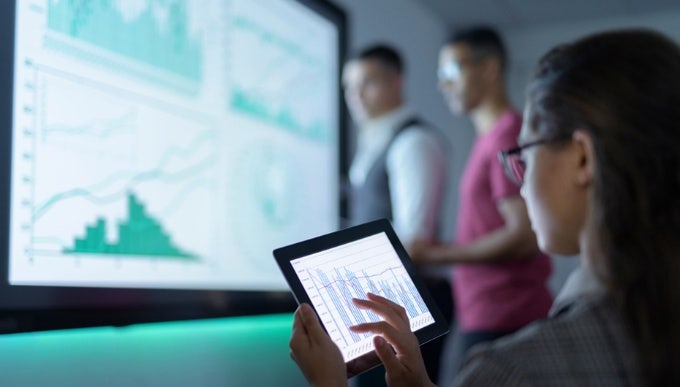 Businesswoman viewing graphs on a digital tablet in a modern office, highlighting Avendra International's data-driven strategic sourcing solutions for the hospitality industry.