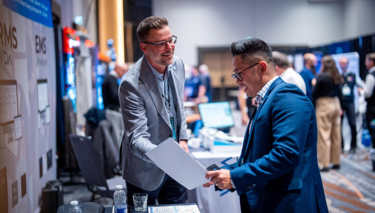 Two men dressed in suits interacting at a conference booth.