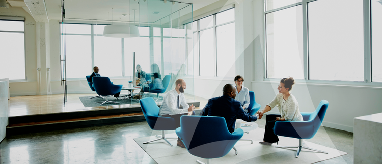 A modern office with blue chairs and large windows, where two groups of people are engaged in discussions in separate areas. A bright, collaborative workspace.