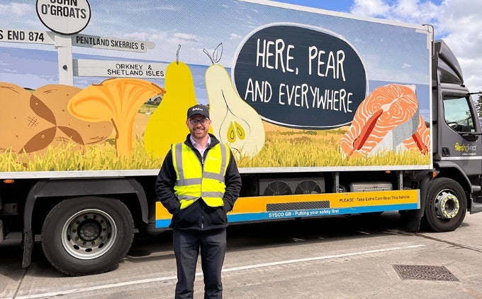 Man wearing safety vest, posing in front of a large commercial truck that says "here, pear and everywhere"