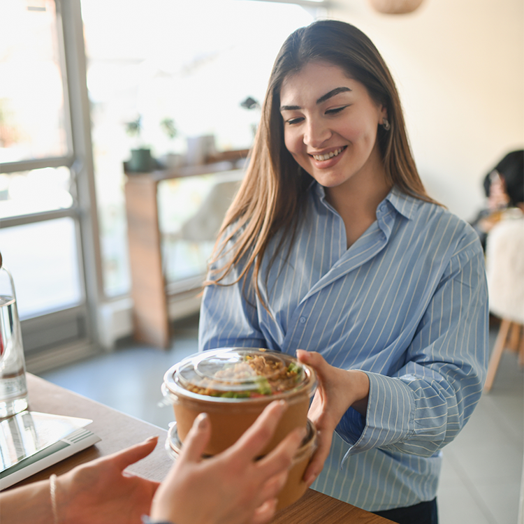 Café staff member handing a takeaway meal to a customer, highlighting grab-and-go dining, convenience food and on-the-go consumption trends.