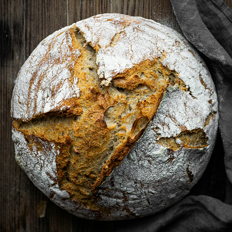 Close-up of rustic artisan sourdough bread loaf on a wooden table, highlighting traditional baking, craftsmanship and authentic food trends.