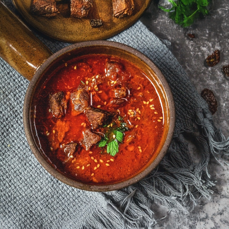 A steaming bowl of red beef stew garnished with green herbs