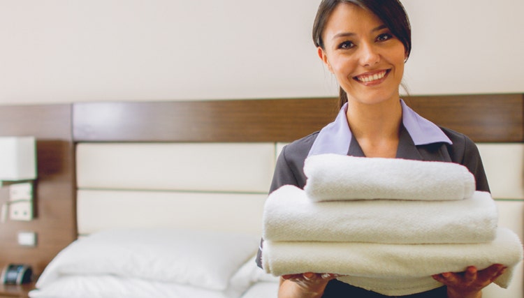 Hotel housekeeper holding fresh folded towels in a guest room, showcasing professional housekeeping services and high hospitality standards.