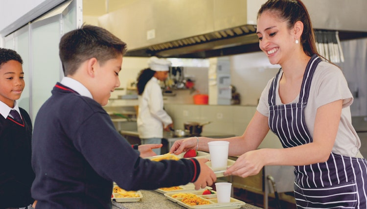 School catering staff serving nutritious hot meals to pupils in a school canteen, representing quality food service and efficient education sector catering support.