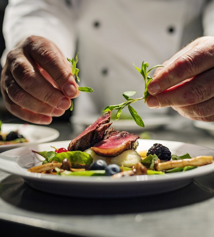 Chef plating and garnishing a steak dish