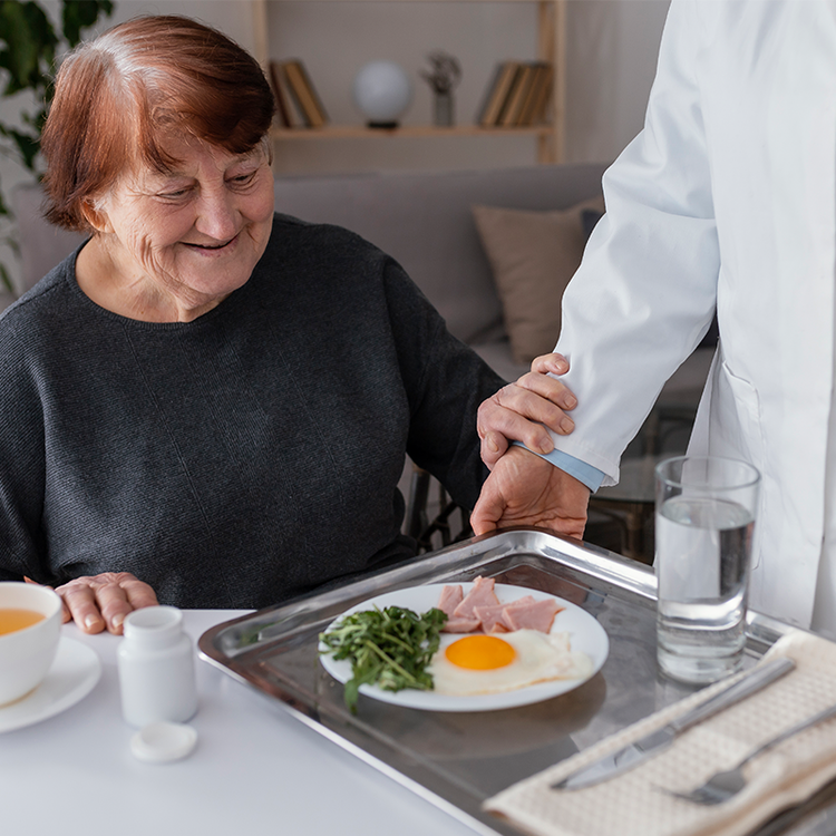 Care assitant serving foor to an elderly lady in a care home