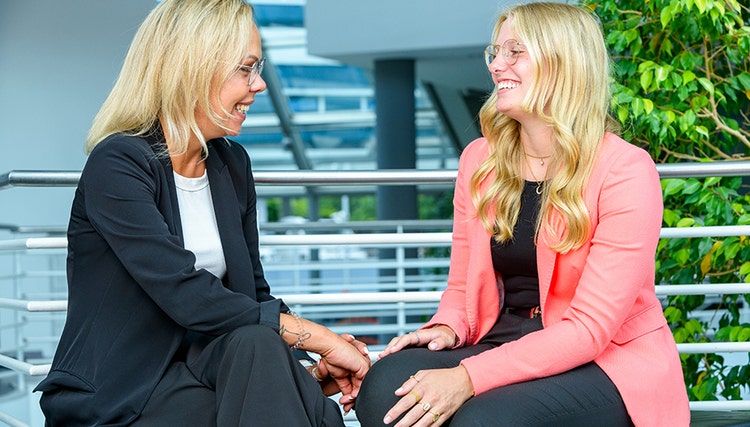 Two women dressed in office attire seated and enaging in a conversation