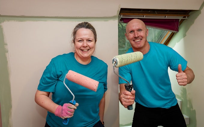 Two painters wearing matching turquoise t-shirts, posing with foam paint rollers in their hands