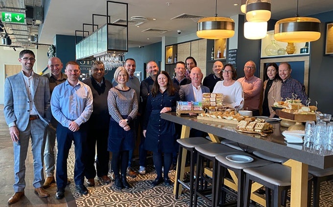 Large group of people smiling and posing for a photo in a modern kitchen / dining area