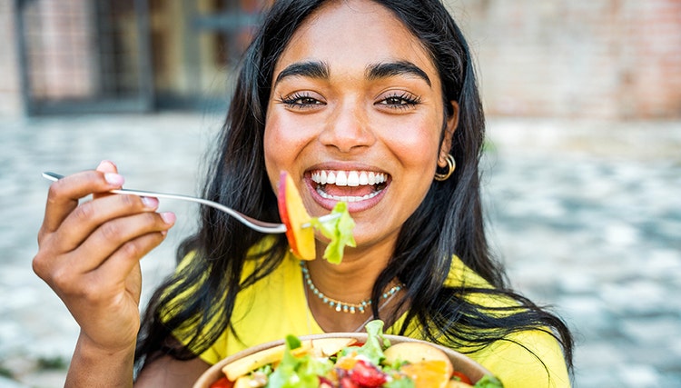 Woman smiling and eating a salad with a fork