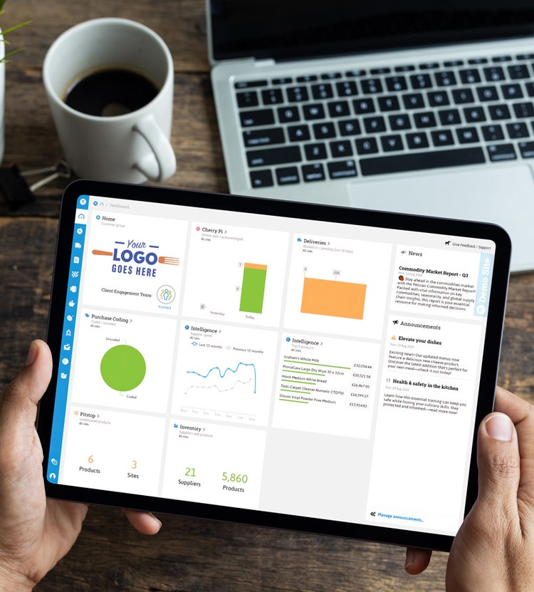 A person holding a tablet with a business dashboard showing colorful charts and graphs, placed above a wooden table with a coffee cup and laptop in the background.