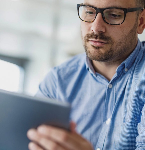 Man wearing glasses and a dress shirt holding a tablet in his hand