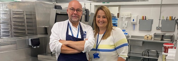 Chef with crossed arms standing in kitchen with smiling woman