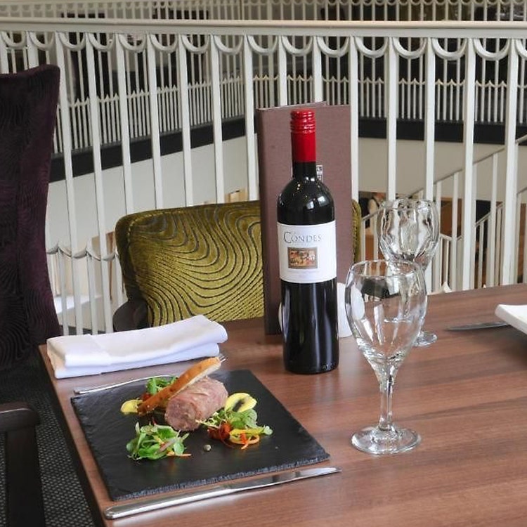A dining table with two plates of food and a bottle of wine