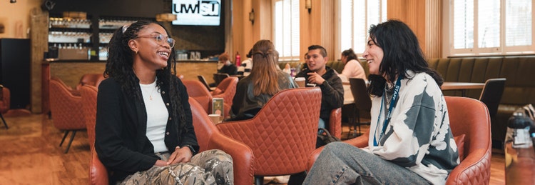 Two women in chairs at a cafe, sharing a moment together, immersed in conversation amidst a warm and inviting ambiance.