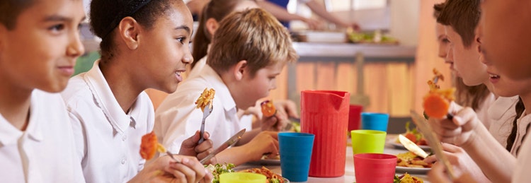 Children in uniforms eating food in a cafeteria