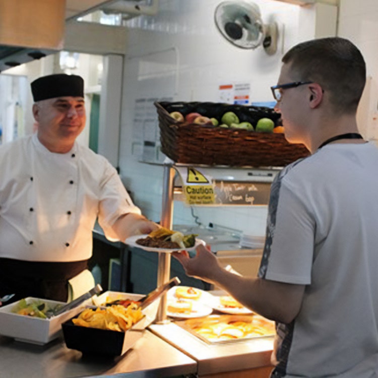 School caterer hands a dish to student