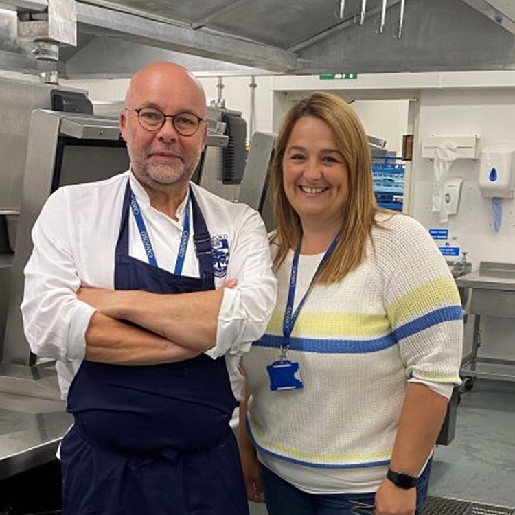 Chef with crossed arms standing in kitchen with smiling woman