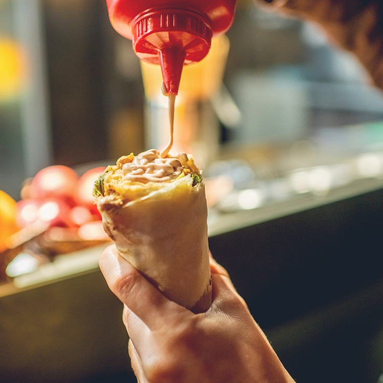 Fresh grab-and-go wrap being prepared with sauce at a foodservice counter