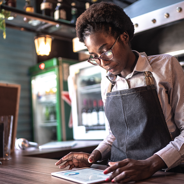 Café worker wearing an apron and glasses using a tablet behind the counter