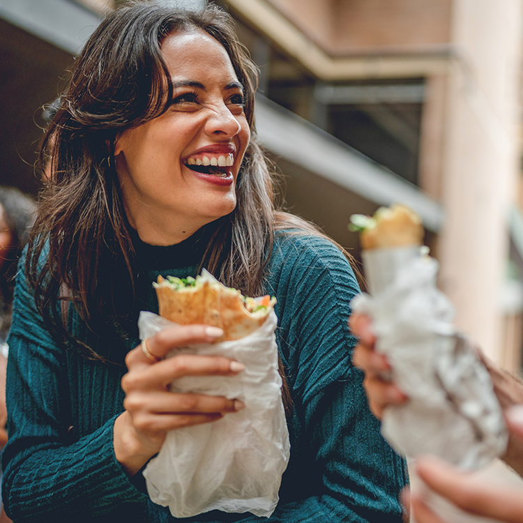 Smiling woman holding a wrapped sandwich while enjoying a casual meal with another person