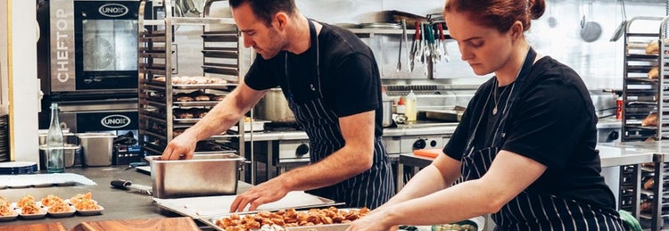 Two chefs collaborate in a bustling kitchen, skillfully preparing various dishes with fresh ingredients.