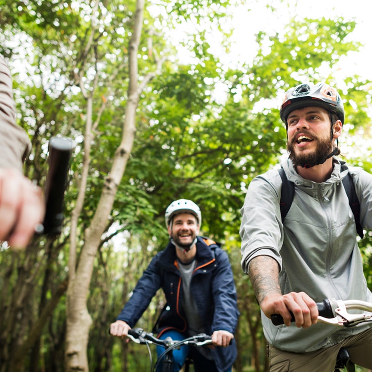Three men cycling through a lush forest, surrounded by trees
