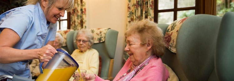 A woman pours orange juice into a glass for an elderly woman, showcasing a moment of care and companionship.