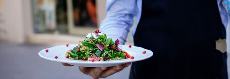 A waiter presenting a plate of fresh salad, showcasing vibrant greens and colorful vegetables.