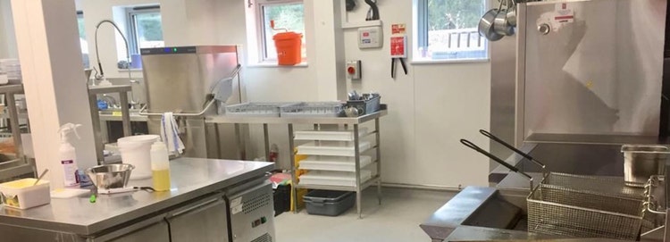 A spacious commercial kitchen featuring modern stainless steel appliances and supplies scattered across countertops