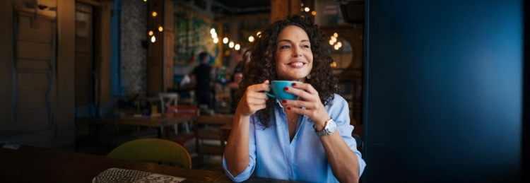 Woman holding a coffee mug smiling inside of a coffee shop