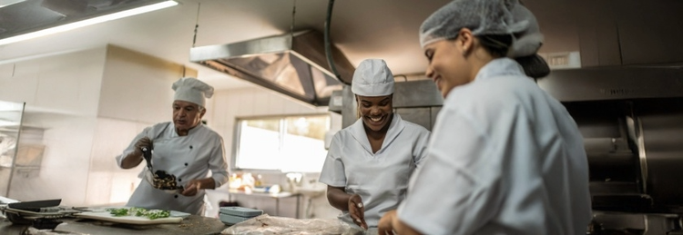 A dynamic kitchen scene featuring three chefs in white uniforms, actively engaged in food preparation and cooking.