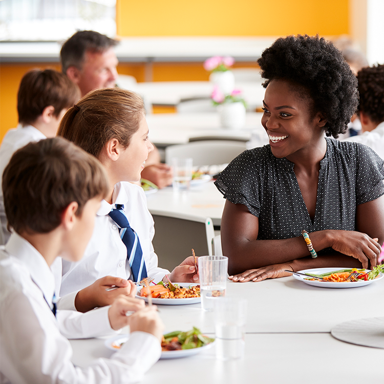 School pupils enjoying a healthy lunch with a member of staff in a school dining hall.
