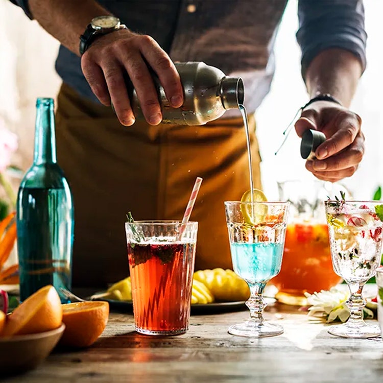 A bartender pours a cocktail into a glass