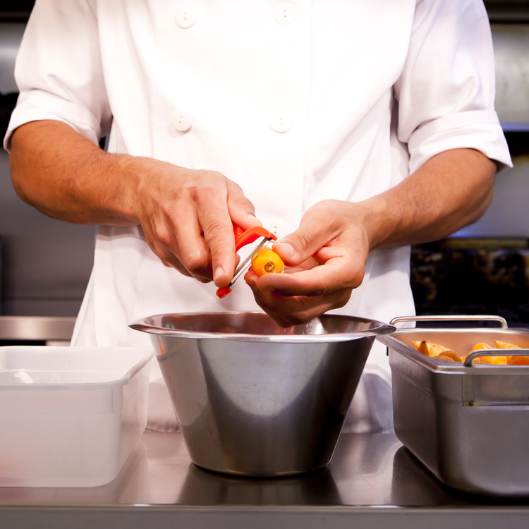 a chef peeling a carrot into a steel bowl