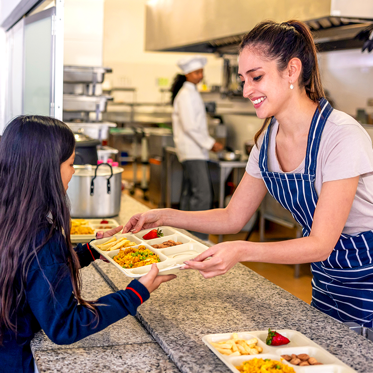 School kitchen worker handing a lunch tray to a primary school pupil.