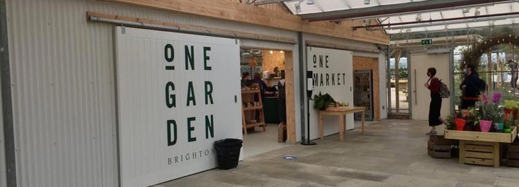 Indoor greenhouse with a small shop. Sliding doors to the entrance of the shop say "One Garden, One Market"