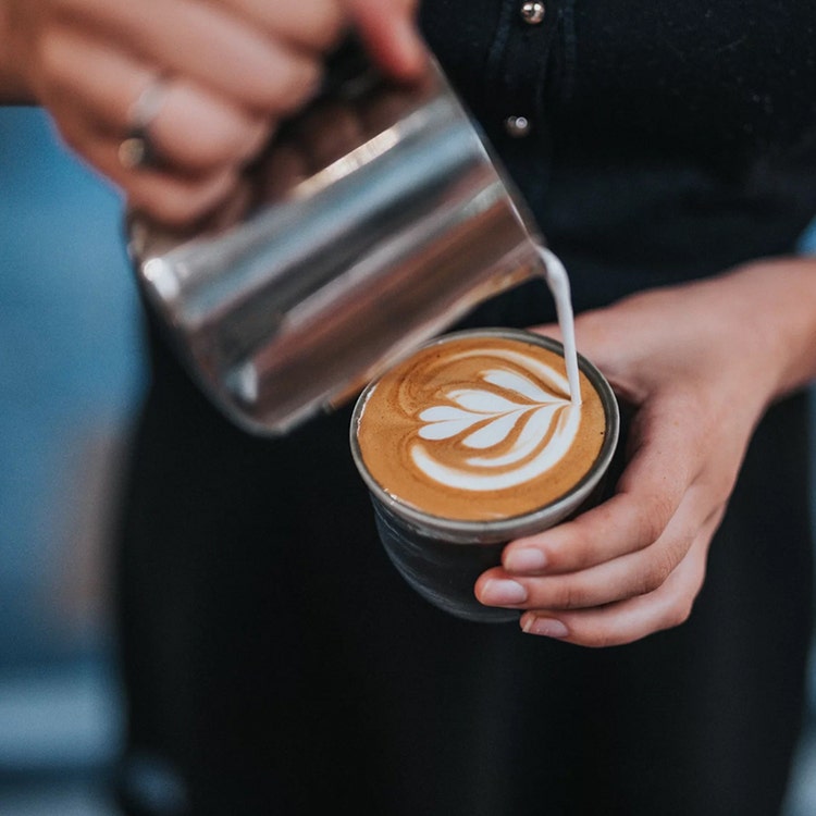 A barista pouring coffee from a pot into a cup.