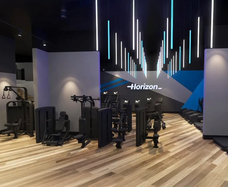 A modern gym with strength training equipment, wooden flooring, and overhead lighting.