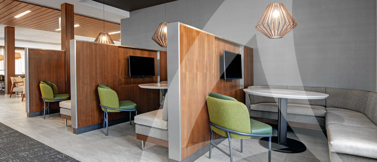 A modern seating area in a public space, featuring wooden booths with mounted screens, round tables, cushioned seating, and green chairs under stylish pendant lights.