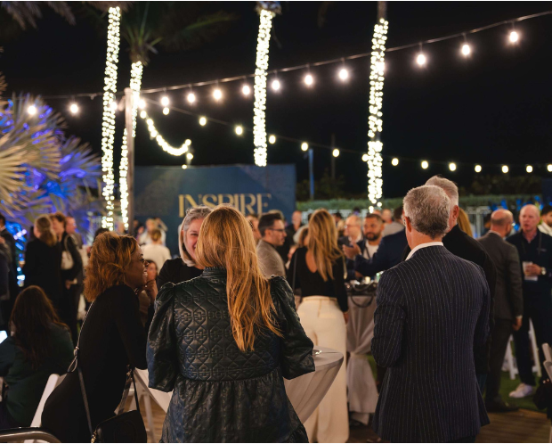 A crowd of people enjoying an outdoor event illuminated by decorative lights in the evening.