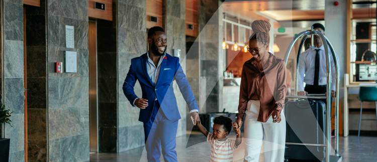 A family with suitcases walks through a hotel lobby with warm lighting.