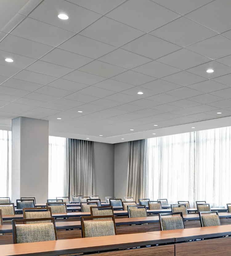 A modern conference or classroom with rows of tables and cushioned chairs, featuring large windows and recessed ceiling lights for a clean, professional look.