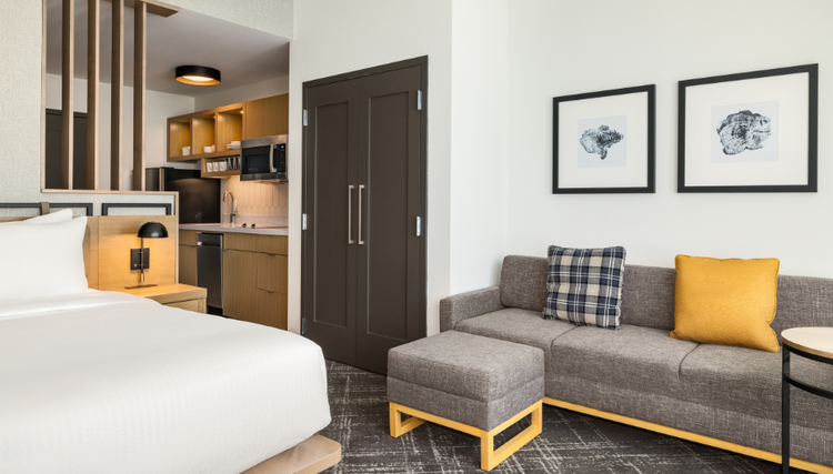 A modern studio apartment with a bed, kitchenette, sofa, and stylish decor, designed for comfort and functionality.