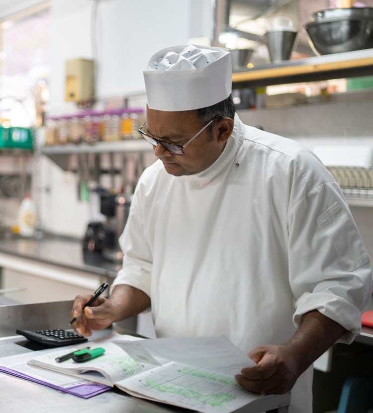 Chef calculating kitchen expenses on a computer at Avendra International, menu planning and cost management