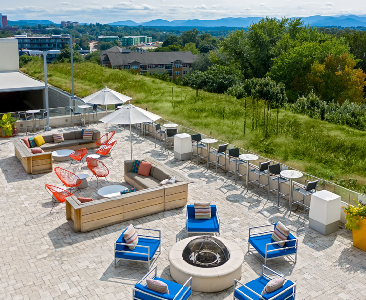 A rooftop patio with colorful seating, a fire pit, and mountain views.